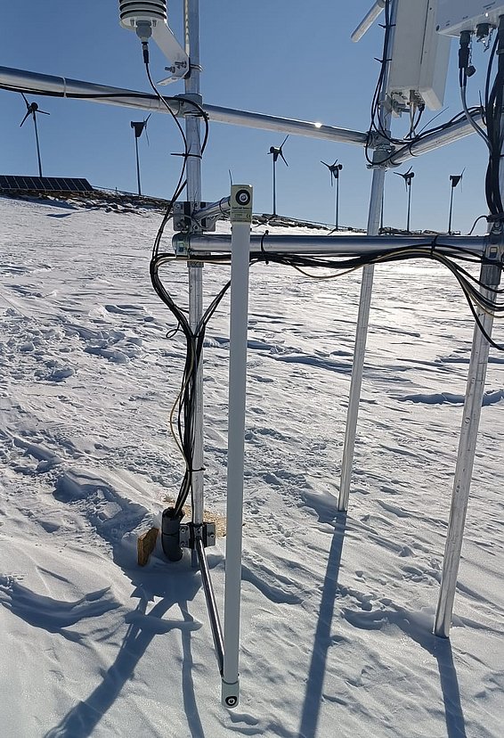 Der FLOWCAPT Messsensor an einem Metallgestell auf schneebedecktem Boden mit Kabeln und Windrädern im Hintergrund
