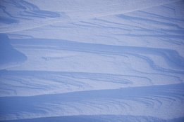 Nahaufnahme von bläulichem Schnee mit wellenförmigen Mustern und Schatten