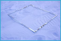 Quadratischer Metallrahmen liegt auf glattem, unberührtem Schnee.