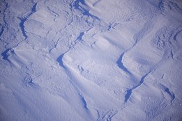 Nahaufnahme von Schnee mit unregelmäßigen Spuren und Vertiefungen im Licht
