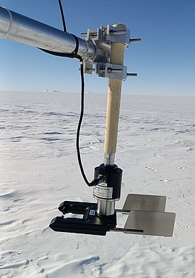 Schneepartikelzähler mit Metall- und Kunststoffteilen an einer Halterung über schneebedecktem Gelände unter klarem Himmel