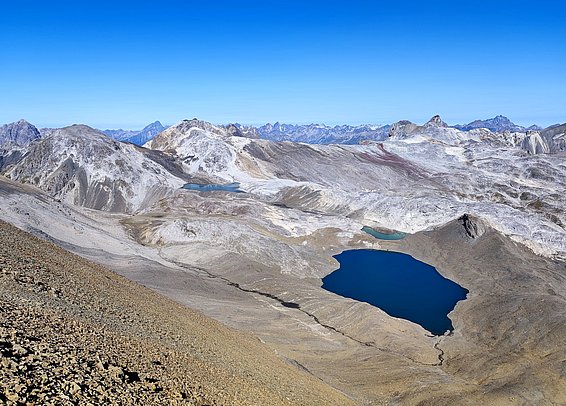 Rugged mountain landscape with clear blue sky. A deep blue lake nestled in rocky terrain, surrounded by jagged peaks.