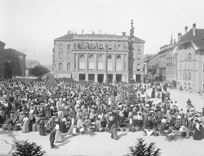 Eine große Menschenmenge versammelt sich auf einem Marktplatz vor dem Bundeshaus in Bern. Das Foto zeigt den Markt im Jahr 1902.