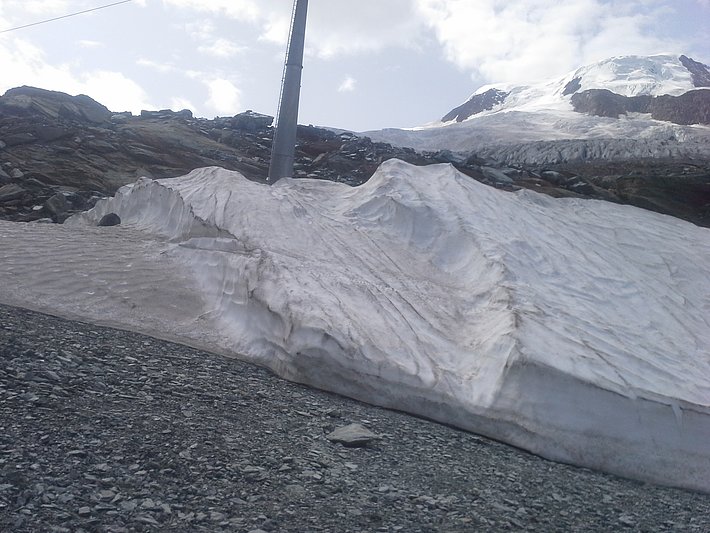 Snowfarming in Saas Fee, VS. Das Bild zeigt den Nutzen einer Vliesabdeckung an einem Nordhang auf 2850 m. Links im Bild der nicht geschützte Bereich. Im Sommer war das Vlies verrutscht und wurde mit einem Bagger nachgerichtet, daher die 2 Stufen (Foto: P. Schneiter, 28.08.2017).