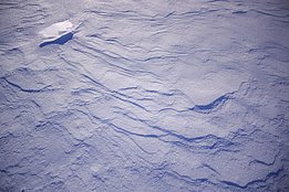Nahaufnahme von schneebedecktem Boden mit sichtbaren Windspuren und Schatten