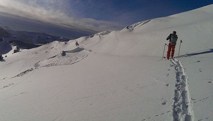 Ein Skitourengänger wandert an einem sonnigen Wintertag in eine schneebedeckte Bergflanke nach oben und hinterlässt eine Spur im Schnee..  