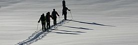 Eine Gruppe von Skitourengänger legt eine frische Spur durch eine ansonsten unberührte Schneedecke.