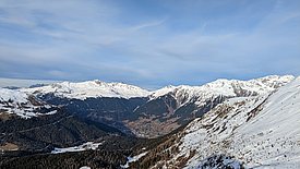 Paysage de montagne avec des sommets enneigés et des vallées boisées sous un ciel nuageux.