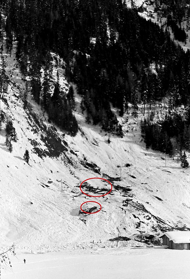 Snow-covered mountain slope with avalanche tracks and two red circled areas