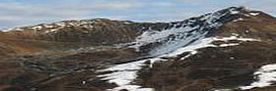 Das Bild zeigt ein alpines Skigebiet in herbstlichen Farben. Nur rund um die Schneelanzen ist der Boden bereits weiss und lässt den Verlauf der Pistenlinie erahnen.