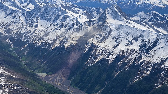 The photo shows an aerial view of the rock and ice avalanche in Blatten, with snow-capped peaks.