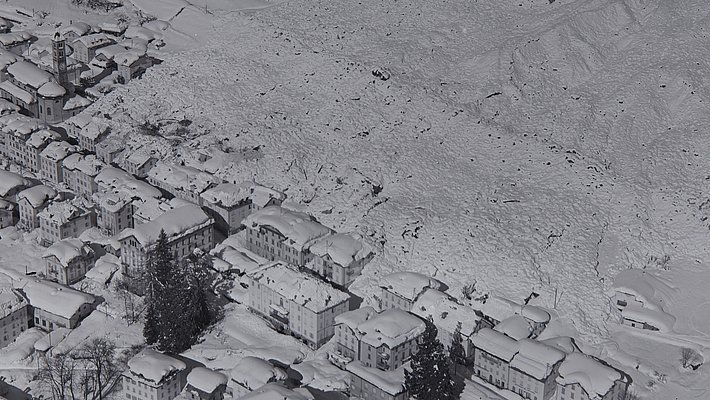 Black-and-white aerial view of an avalanche cone on a mountainside next to a village with buildings and roads