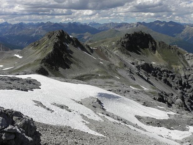 Abb. 4: Allgemein wenig Schnee lag Ende Juni noch in hohen Lagen im Umbrail-Gebiet (Val Müstair, GR). Ausnahme bildeten ausgeprägte, nordseitig Rinnen oder wie im Bild Wächten, wo der Wind während des Winters viel Schnee abgelagert hatte. Hier hätte die Schneemenge wohl sogar noch für den Bau eines Biwaks ausgereicht. Blick vom P. Umbrail (3033 m) nach Nordwesten Richtung Ofenpass (links im Bild) und Fluchthorn (3398 m, Bildmitte ganz im Hintergrund; Foto: SLF/Th. Stucki, 26.06.17).