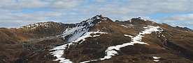 Das Bild zeigt ein alpines Skigebiet in herbstlichen Farben. Nur rund um die Schneelanzen ist der Boden bereits weiss und lässt den Verlauf der Pistenlinie erahnen.