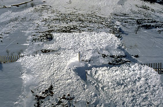 Schneebedecktes Feld nach einem Lawinenabgang mit unregelmäßigen Schneeflächen und teilweise sichtbarem Boden