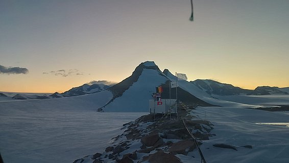 Antarktische Landschaft mit schneebedeckten Bergen und einer kleinen Forschungsstation bei dämmrigem Licht im Februar während der antarktischen Nacht