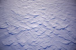 Nahaufnahme von unebenem, schneebedecktem Boden mit sichtbaren Strukturen und Schatten