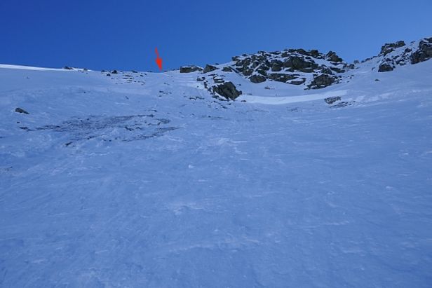 Abb. 9: Blick von unten zum Anriss der Schneebrettlawine von Abbildung 8. Der rote Pfeil markiert erneut die Einfahrtspur des Skifahrers, welcher die Schneebrettlawine ausgelöst hat. Im Bereich des Anrisses und links sieht man eindeutig, dass die Schneebrettlawinen in bodennahen Schichten der Schneedecke, also im Altschnee angebrochen ist (Foto: J. Ender, 19.02.2017). 
