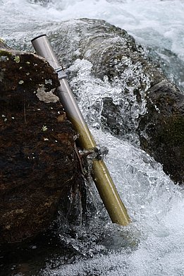 A metal tube attached to a rock, surrounded by splashing water.