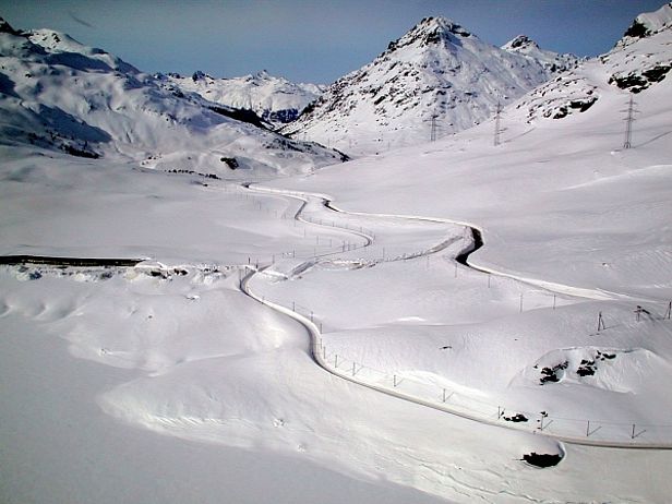 Abb. 21: Piz Lagalp und Berninastrecke nördlich des Berninapasses. Die Rhätische Bahnstrecke (links) und die Passstrasse (rechts) führen durch meterhohe Schneeschluchten. Die von den Schneeschleudern der Bahn ausgeworfenen Schneemassen (im Vordergrund links) sind enorm (Foto: SLF / T. Wiesinger, 12.02.2001).