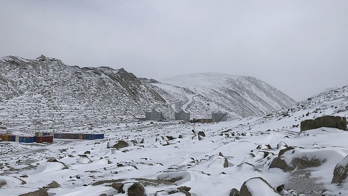 Eine verschneite bergige und steinige Landschaft. Im Tal sind Wohncontainer zu sehen.