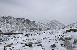 Eine verschneite bergige und steinige Landschaft. Im Tal sind Wohncontainer zu sehen.