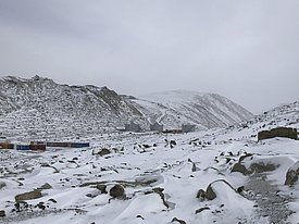 Eine verschneite bergige und steinige Landschaft. Im Tal sind Wohncontainer zu sehen.