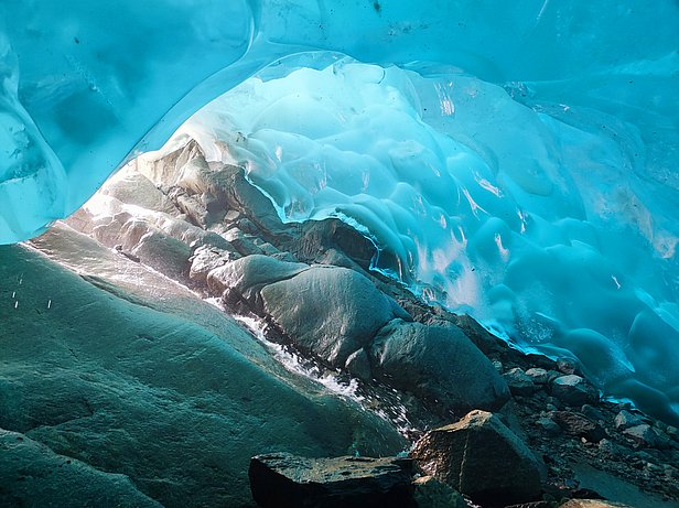 Blick aus einer Eishöhle mit glatten, bläulichen Eiswänden und Felsen am Boden