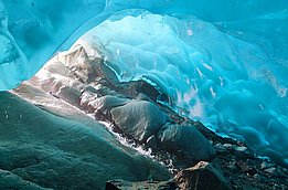 Vue depuis une grotte de glace aux parois lisses et bleuâtres et au sol rocheux