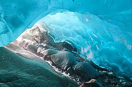 Blick aus einer Eishöhle mit glatten, bläulichen Eiswänden und Felsen am Boden
