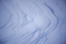 Nahaufnahme von Schnee mit wellenförmigen, bläulichen Schattenmustern