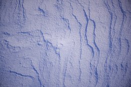 Nahaufnahme von Schnee mit Linien und Spuren, die durch Bewegung oder Wind entstanden sind.