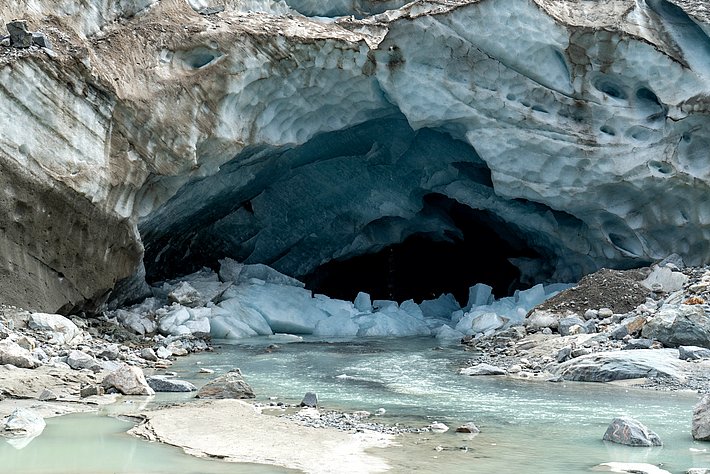 Ice cave at Morteratsch Glacier with flowing meltwater and rocky shore.