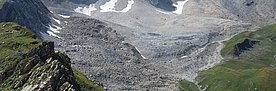 Blockgletscher oberhalb der Alp Flix. Der Blockgletscher selbst sieht aus wie eine Geröllhalde. Allerdings wird das Gestein durch die Vergletscherung so befestigt,  dass die Neigungswinkel viel steiler sind als bei lockerem, frei liegendem Geröll. Der grau-beige Blockgletscher ist links und rechts von grünen Hängen eingerahmt.